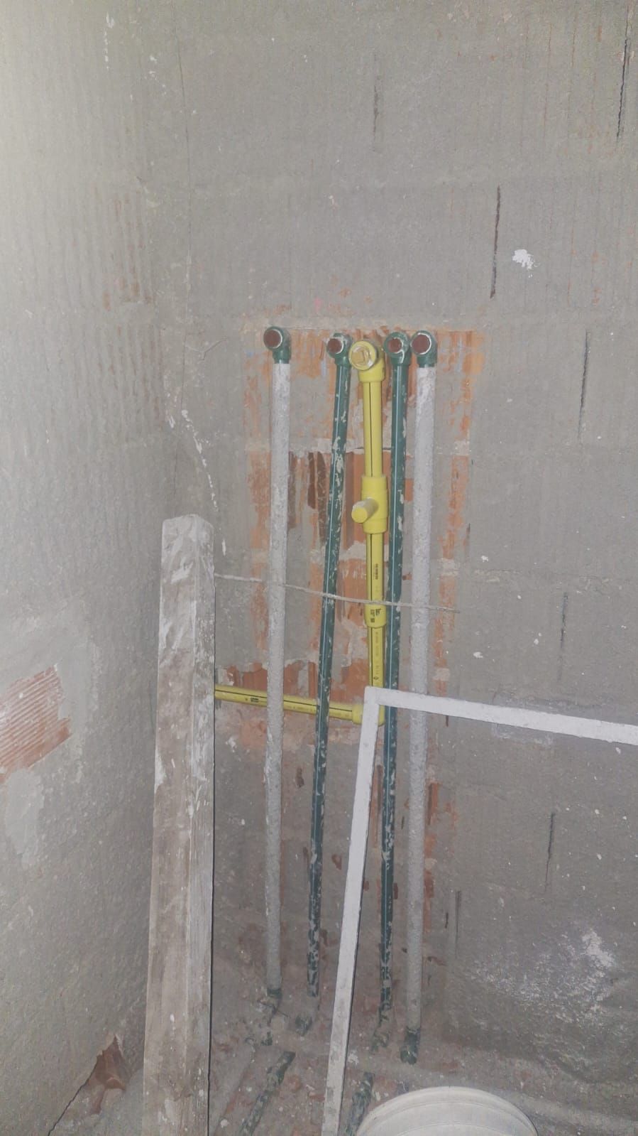 Tuberías de varios colores, incluidos blanco, verde y amarillo, instaladas en un hueco de una pared de ladrillos