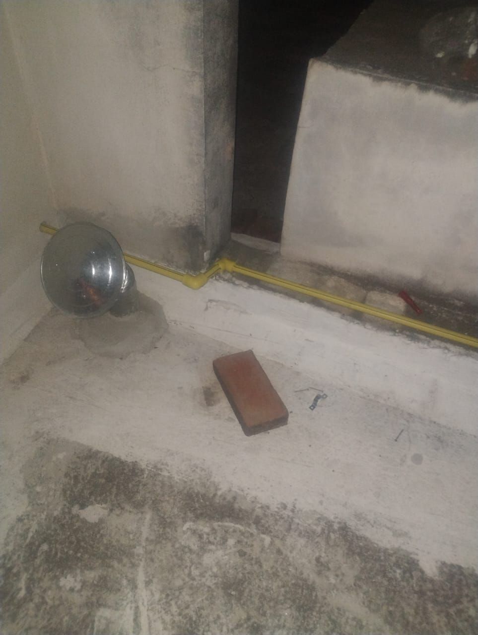 Luminaria de ladrillo y metal sobre suelo de hormigón con conducto amarillo a la vista.