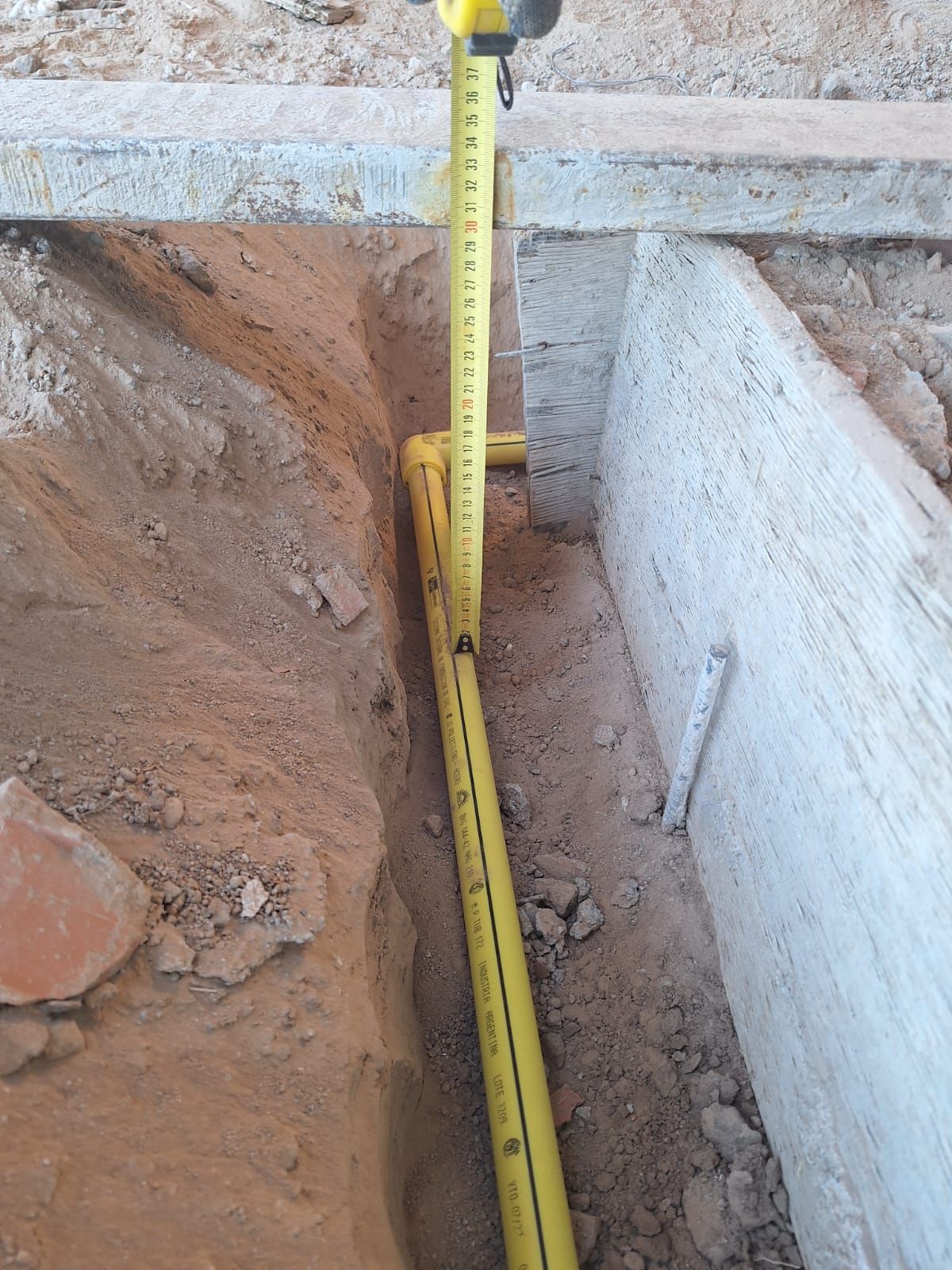 Una cinta métrica amarilla en una zanja estrecha al lado de una estructura de hormigón; midiendo.