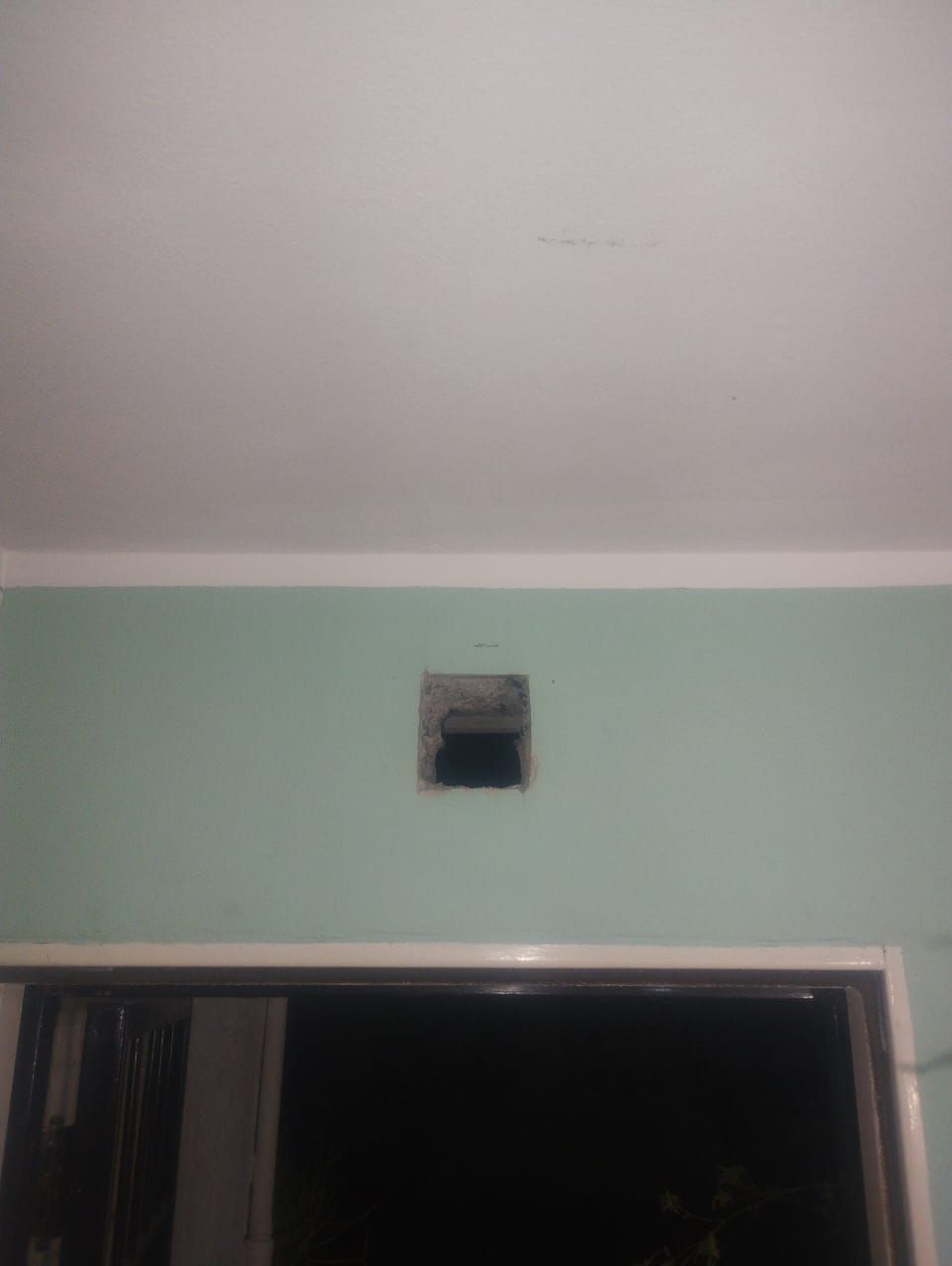 Abertura cuadrada en muro verde sobre portal, techo y moldura blancos.