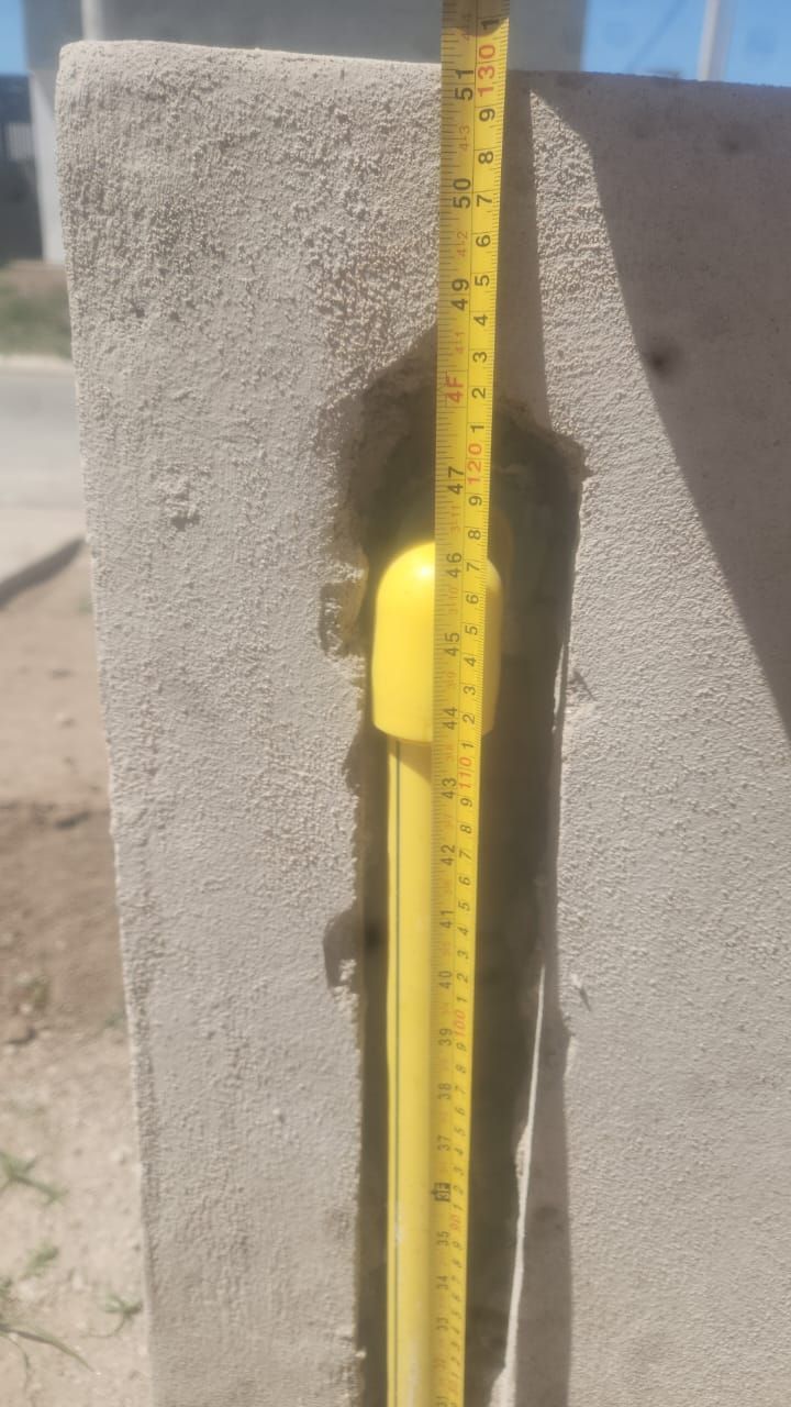 Cinta métrica amarilla junto a un tubo amarillo incrustado en un poste de hormigón.