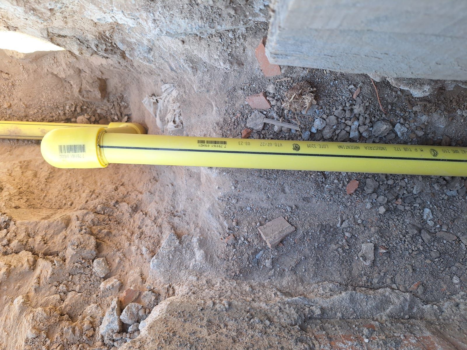 Tubería de gas amarilla enterrada en una zanja, cerca de una estructura de hormigón.