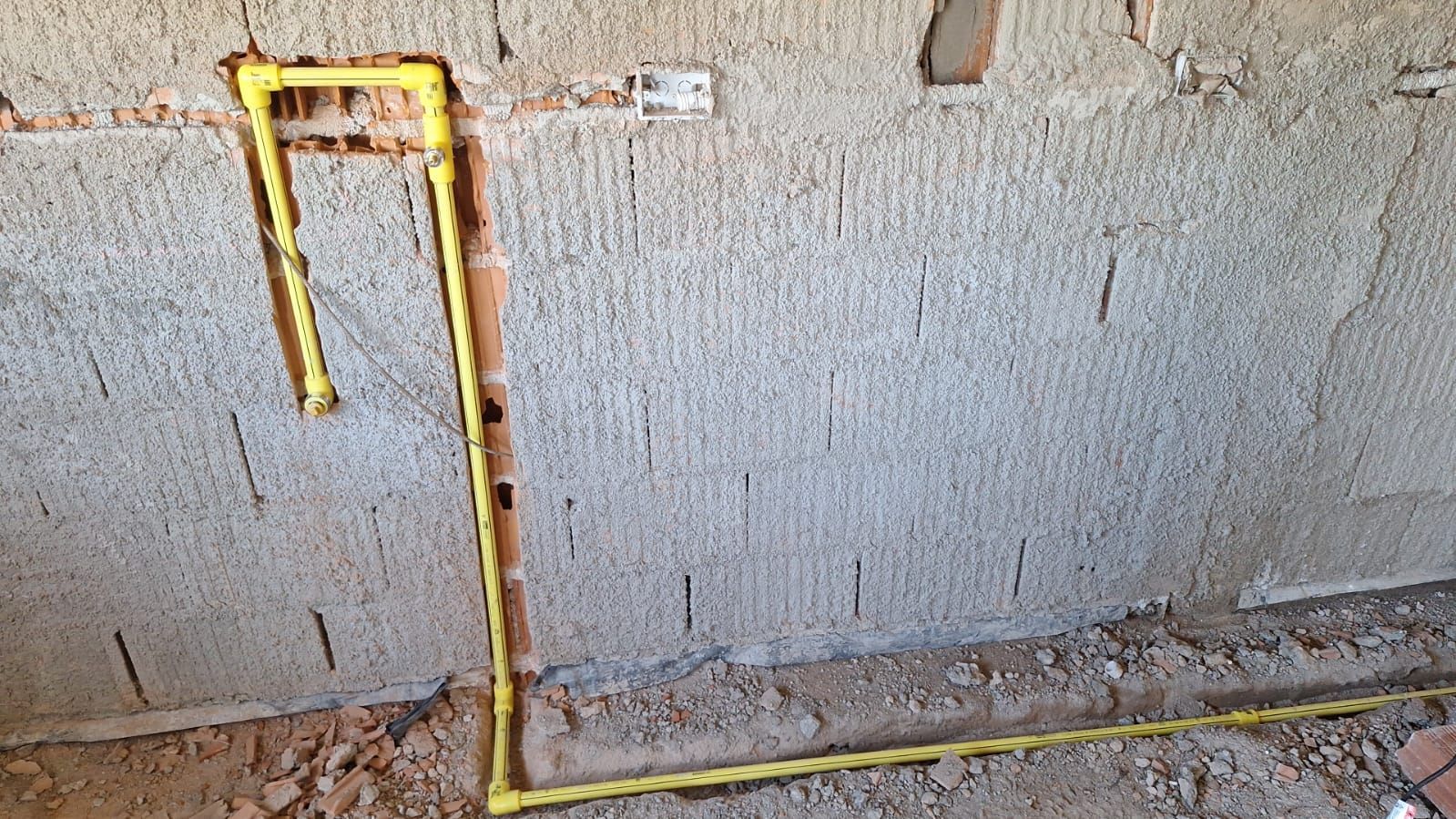 Tubos amarillos incrustados en una pared rugosa, probablemente para plomería durante la construcción.