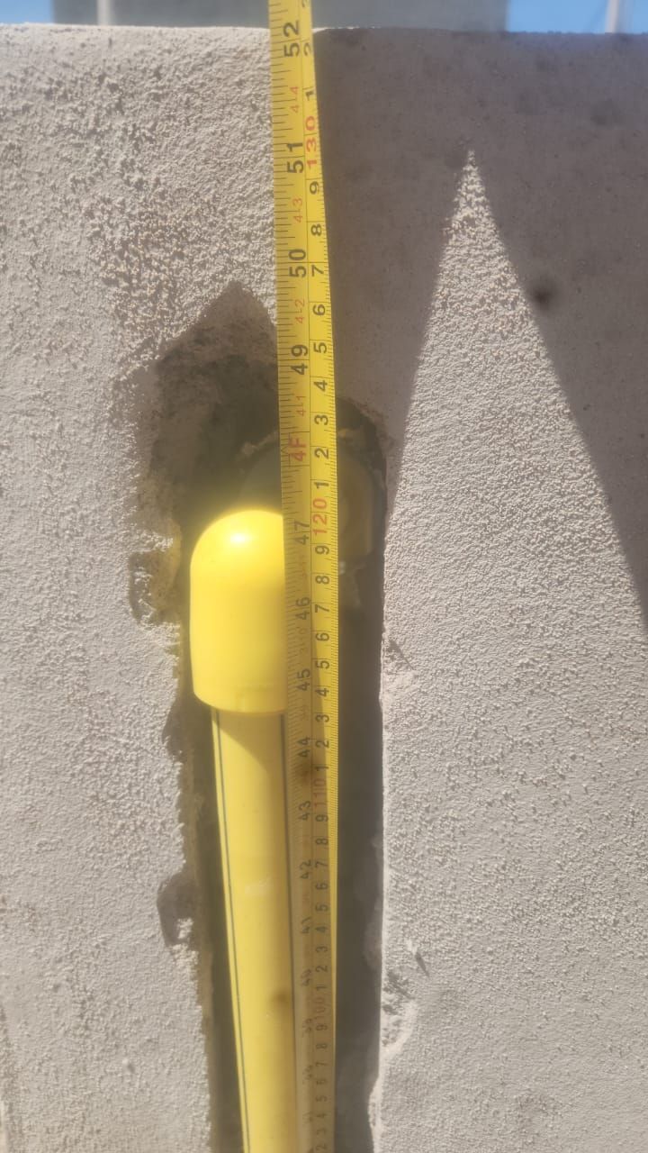 Tubo con tapa amarilla y cinta métrica amarilla en una pared de hormigón empotrada.