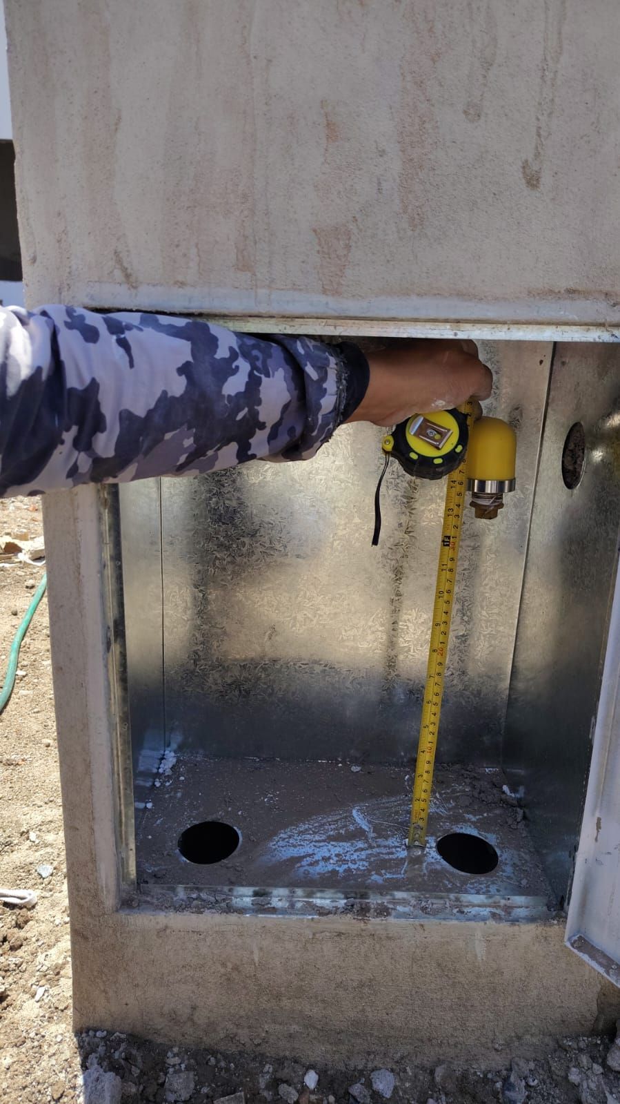 Persona midiendo dentro de una caja de metal con una cinta métrica amarilla al aire libre.
