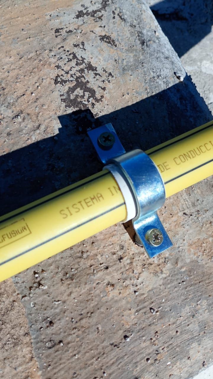Tubo amarillo fijado a una superficie de hormigón con una abrazadera metálica y tornillos.