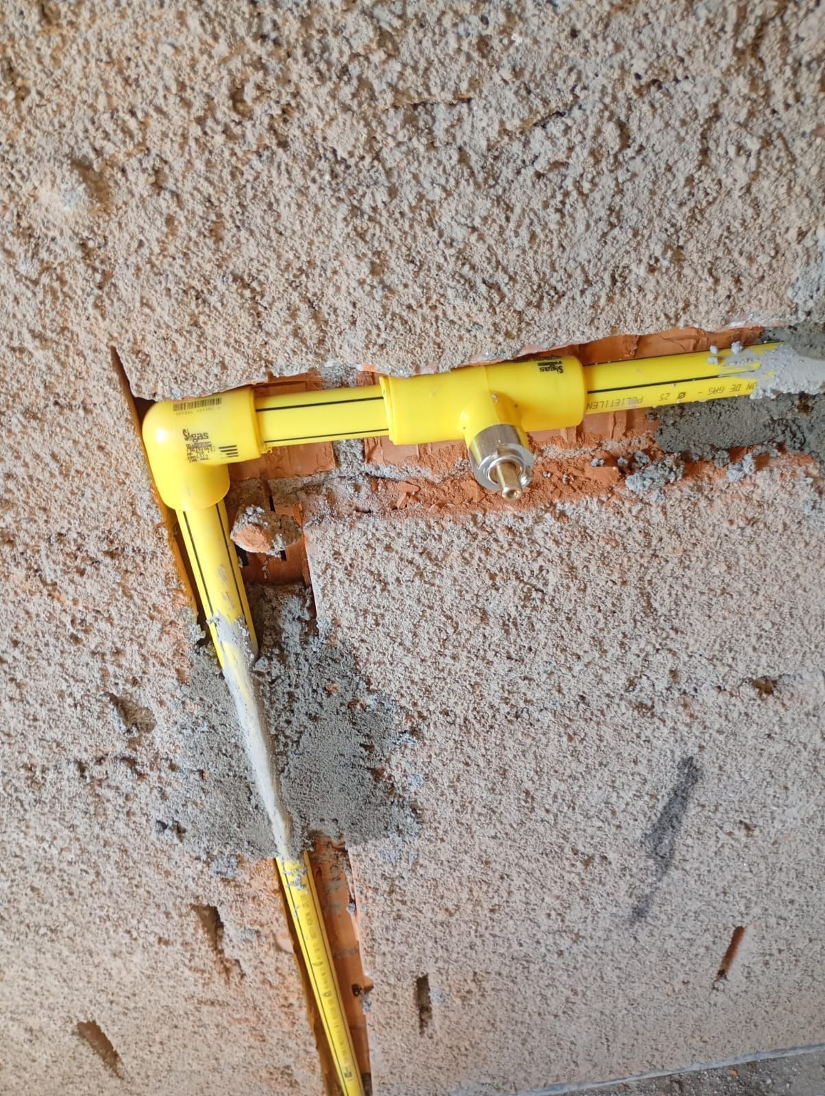 Tuberías de gas de color amarillo instaladas en una pared de hormigón, con válvula metálica.