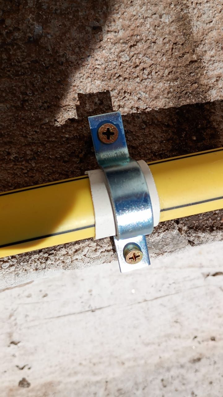 Tubo de gas amarillo fijado a una pared de piedra con una abrazadera de metal y tornillos.