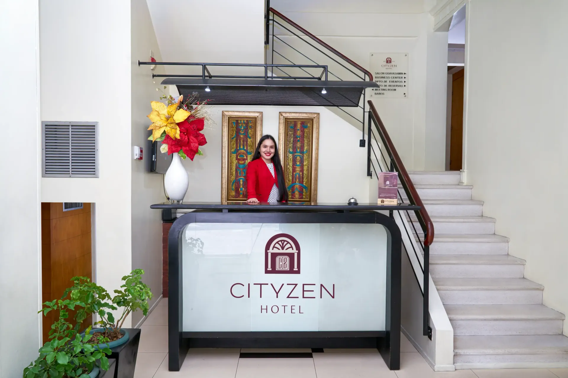 A woman in a red jacket is standing at a cityzen hotel reception desk.