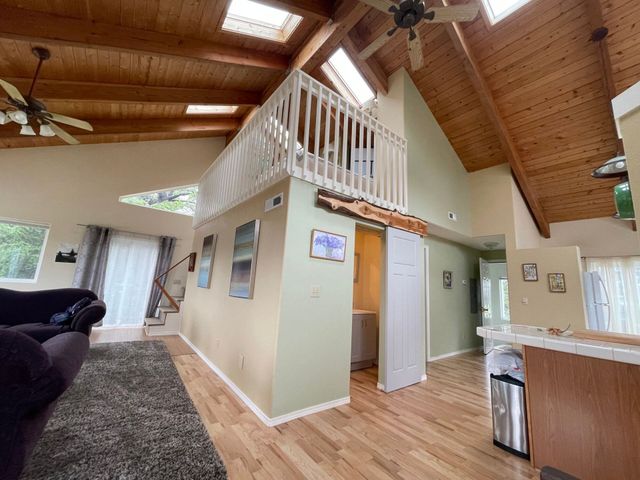 A vaulted living room with a loft area, wood ceiling, skylights, light green walls, and hardwood floors.