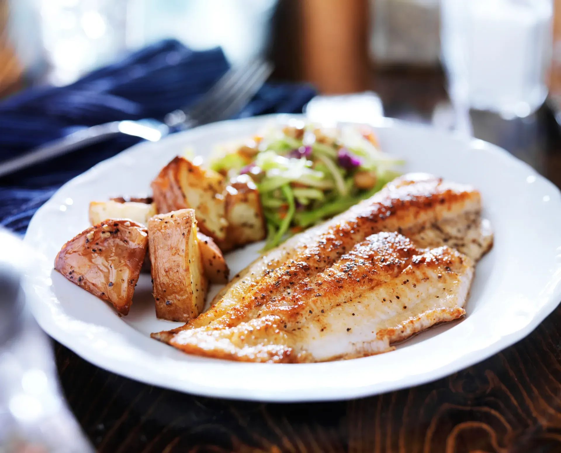 A plate featuring a golden-brown seasoned fish fillet, roasted potato wedges, and a fresh green salad.