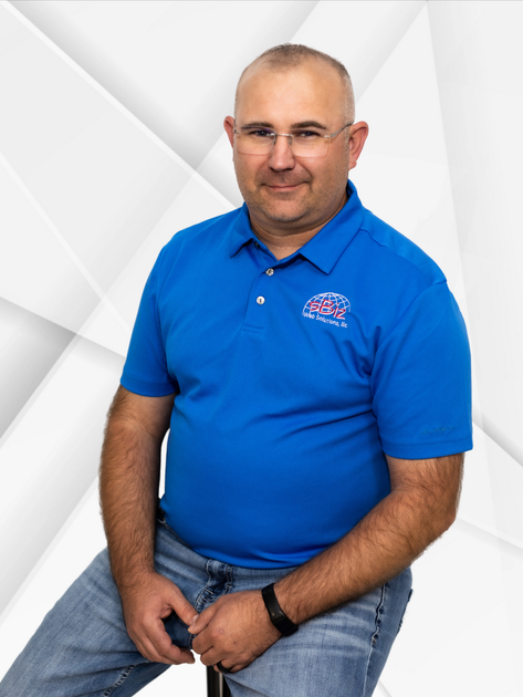 A man wearing a blue shirt and jeans is sitting on a stool.