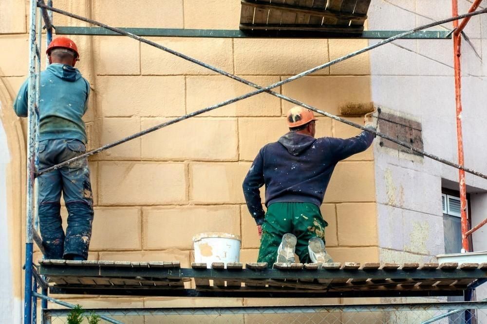 Two painters on scaffolding, painting a building. One applies paint with a roller; the other watches.