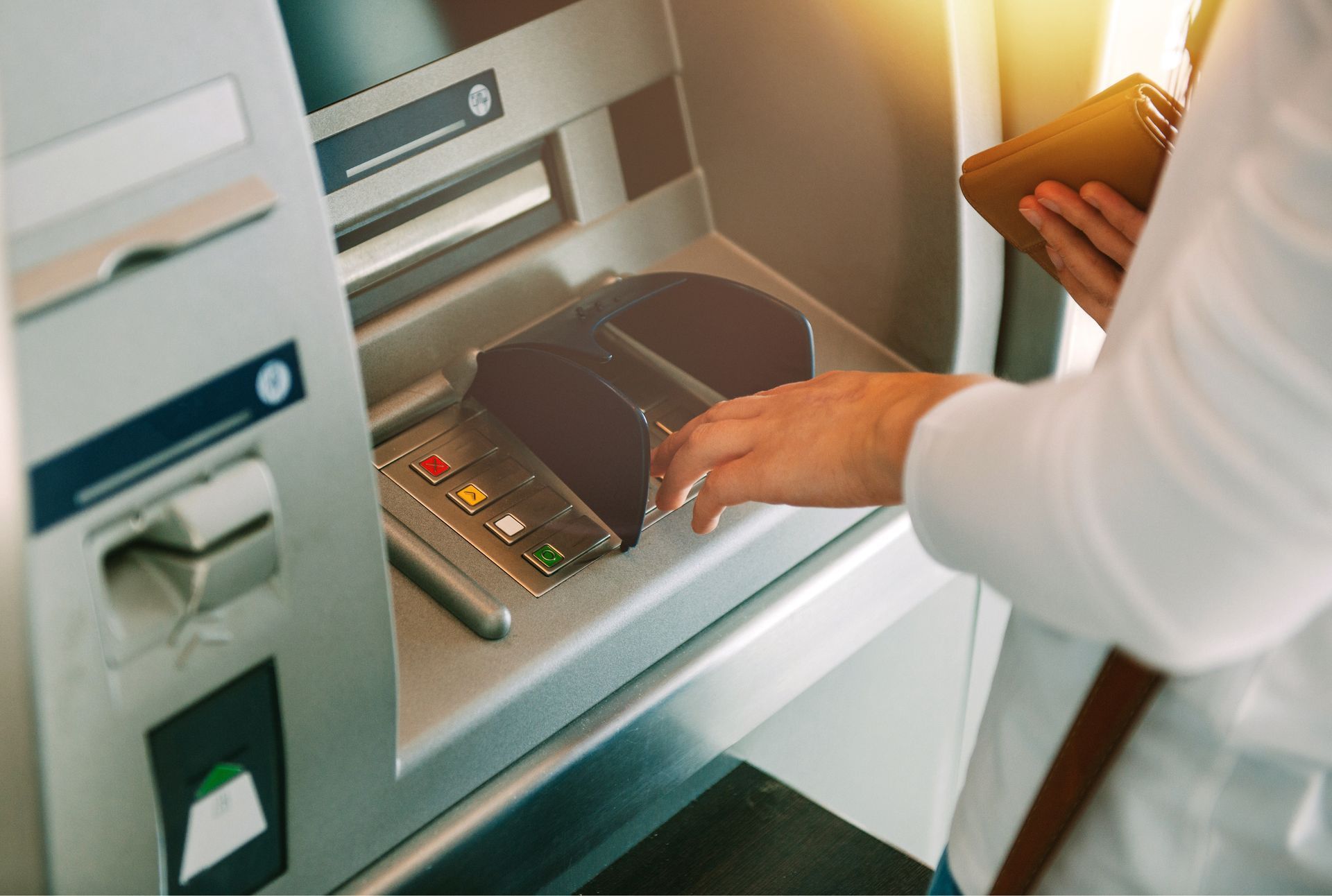 A person is using an atm machine while holding a wallet.