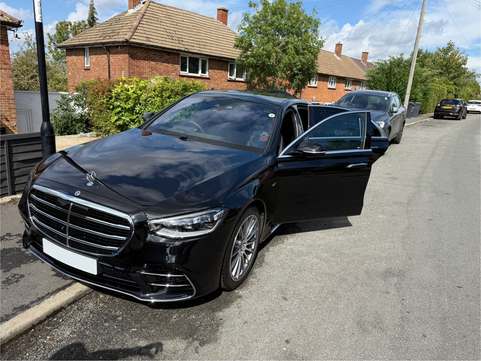 Black Mercedes-Benz sedan parked on a residential street; door open.