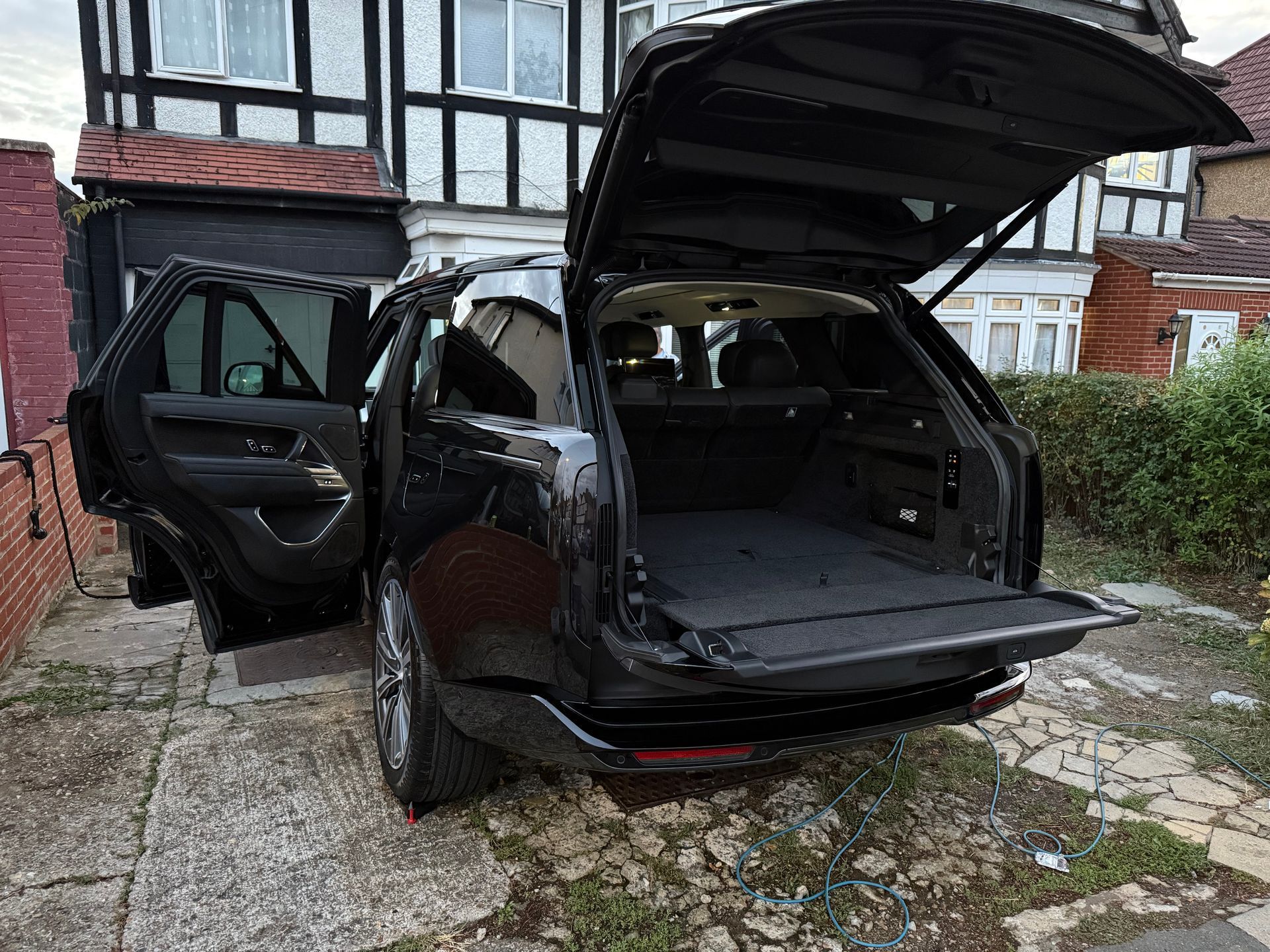 Black Range Rover SUV with open doors and trunk, parked on a driveway.