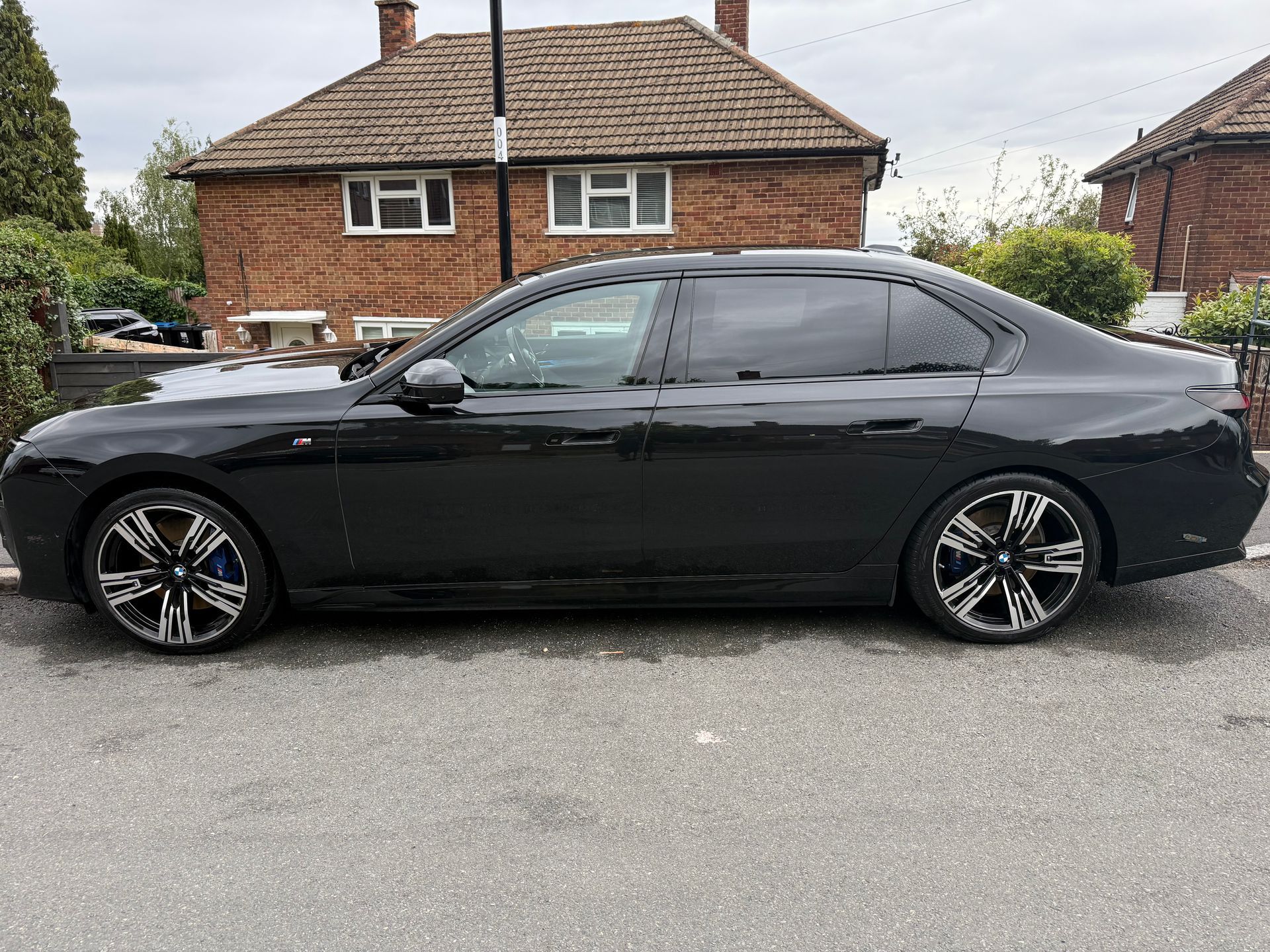 Black sedan parked on a street in front of a brick house.