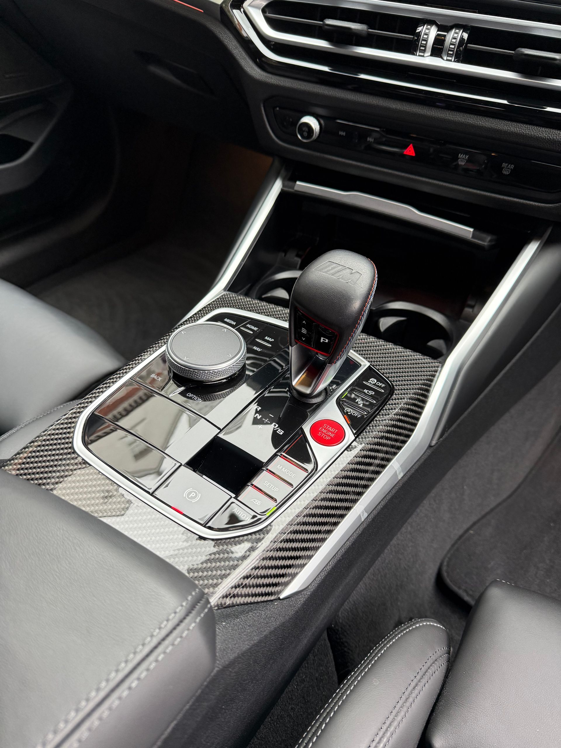 Carbon fiber car console with gearshift and red M button.