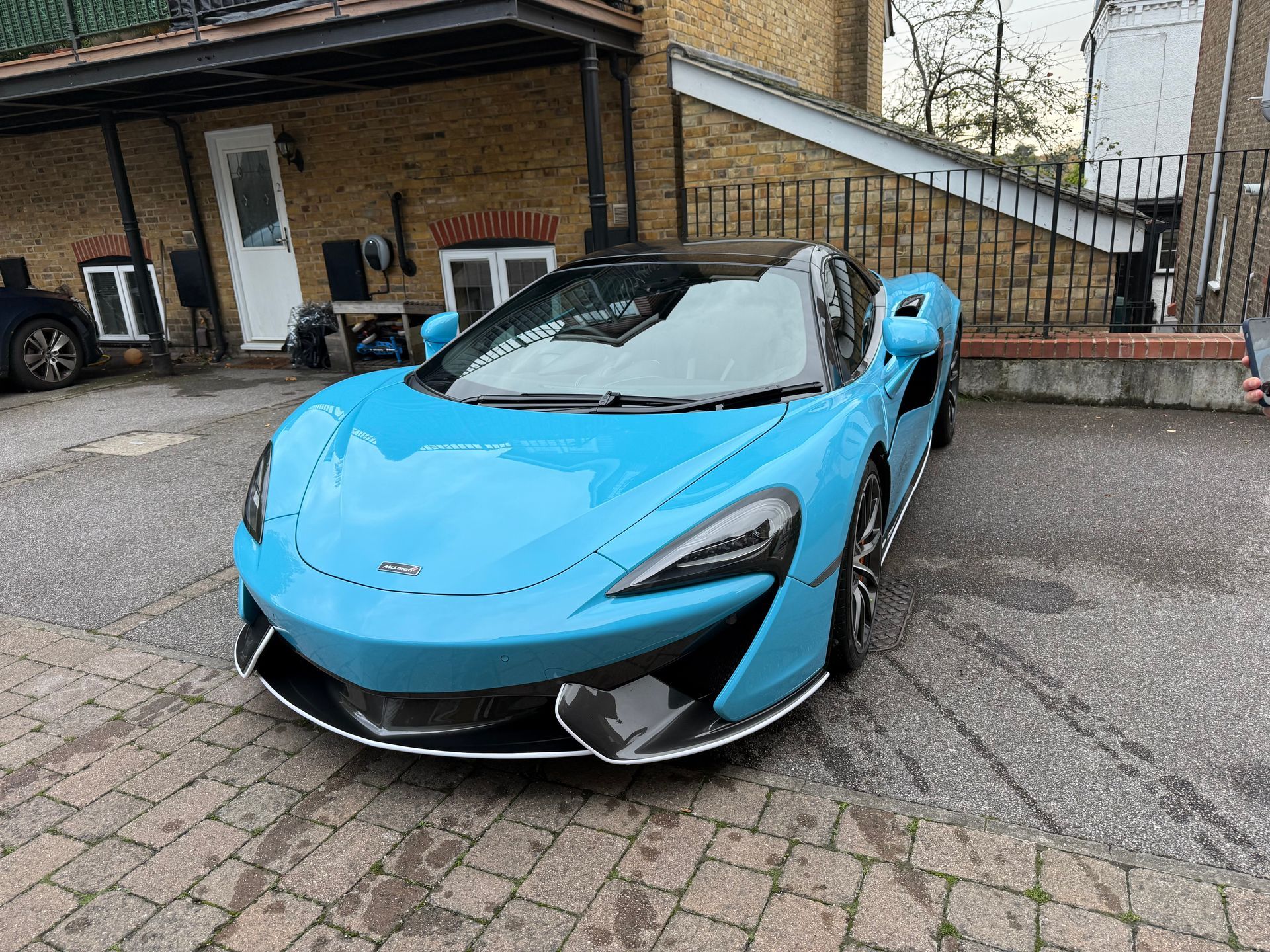 Blue McLaren sports car parked on cobblestone.