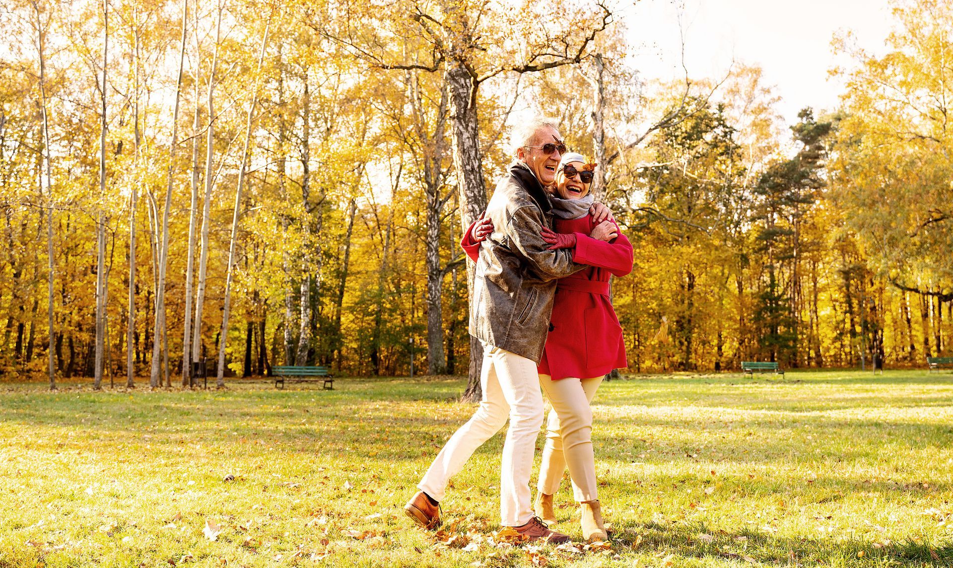 An elderly couple is hugging each other in a park.