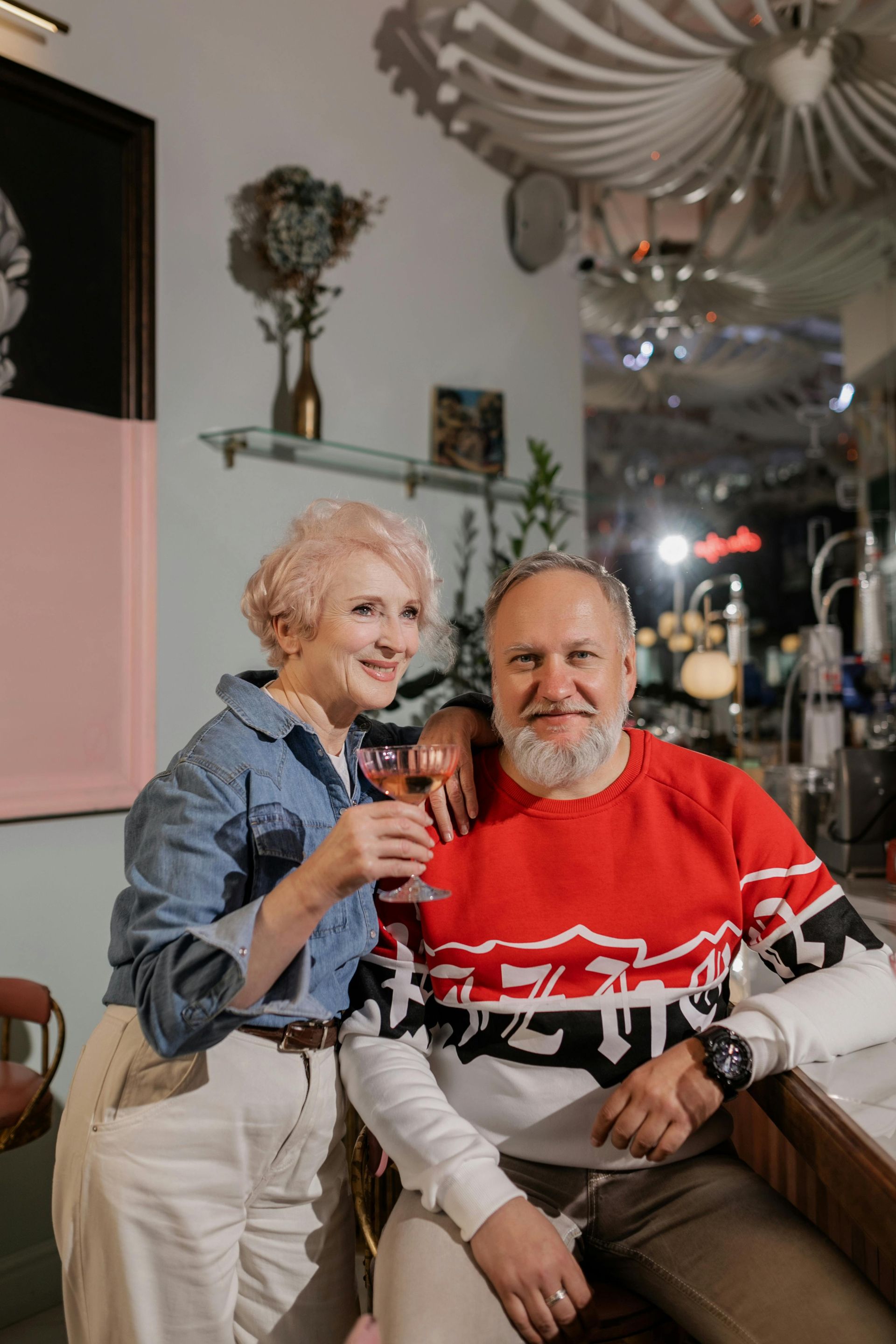 An elderly couple is sitting at a bar drinking wine.