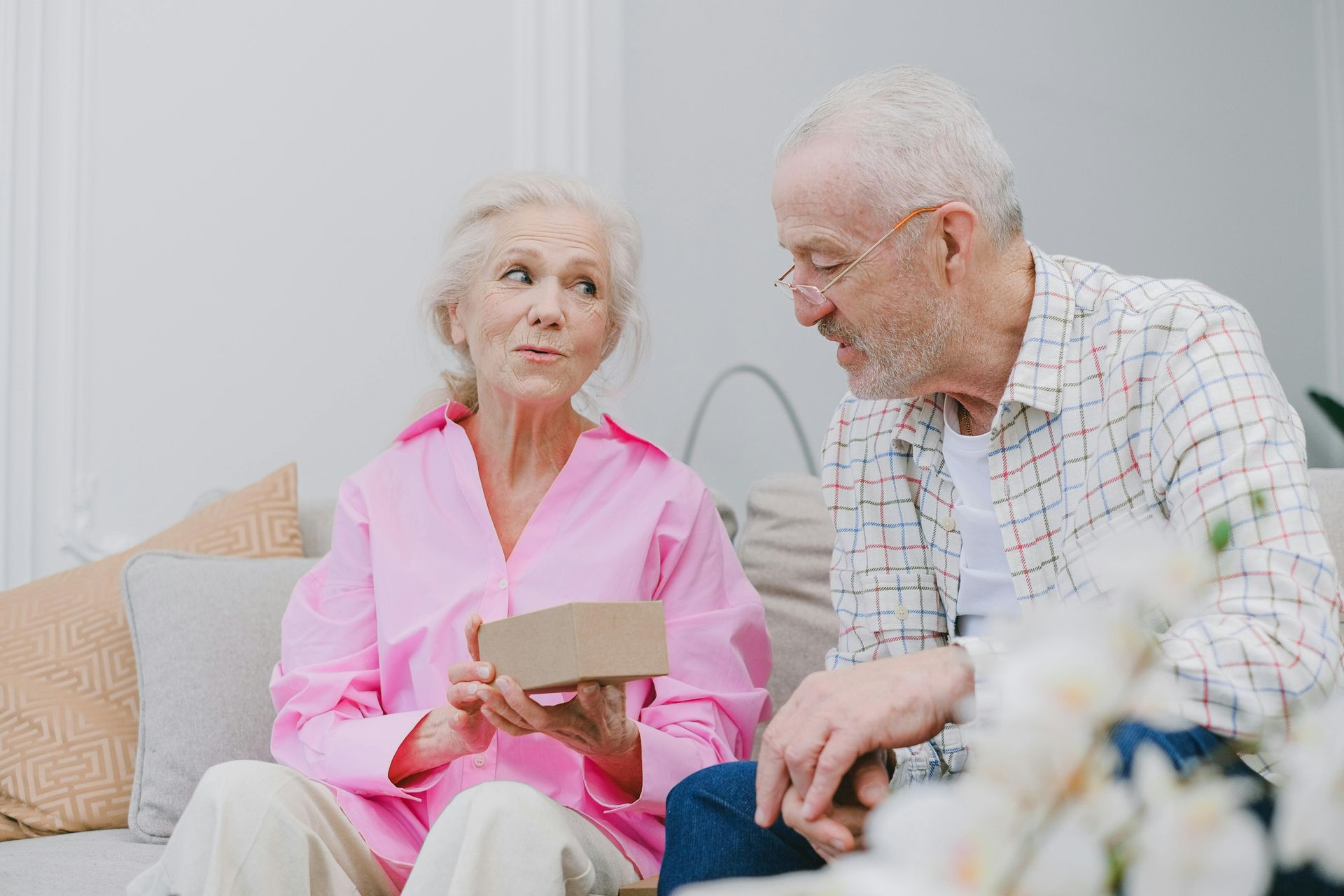 An elderly couple is sitting on a couch looking at a card.
