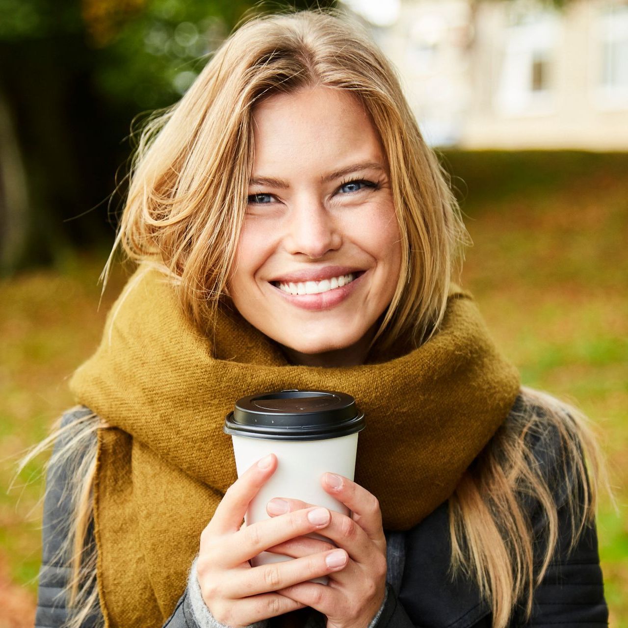 A woman wearing a scarf is smiling while holding a cup of coffee