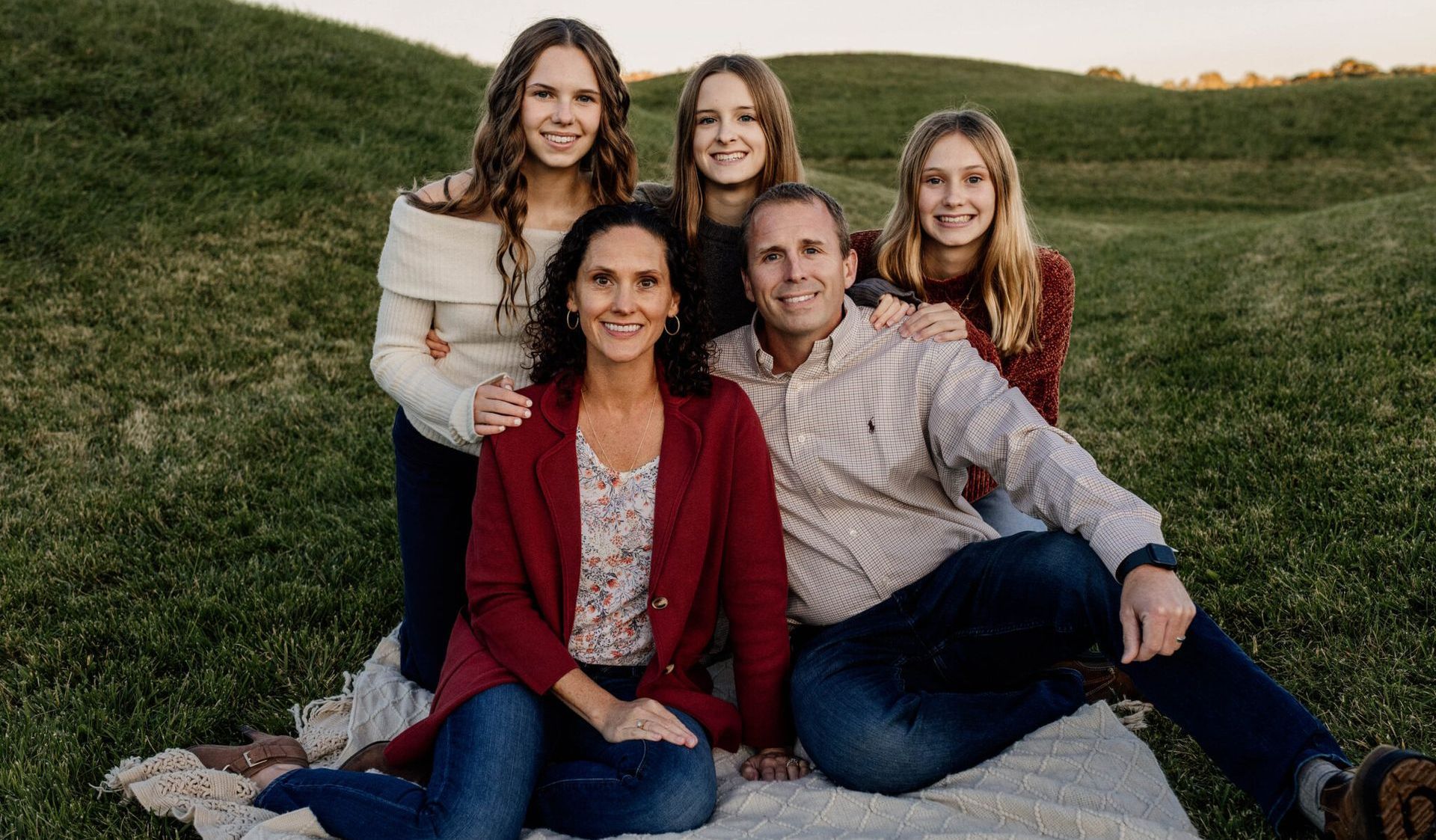 A family is posing for a picture while sitting on a blanket in the grass.