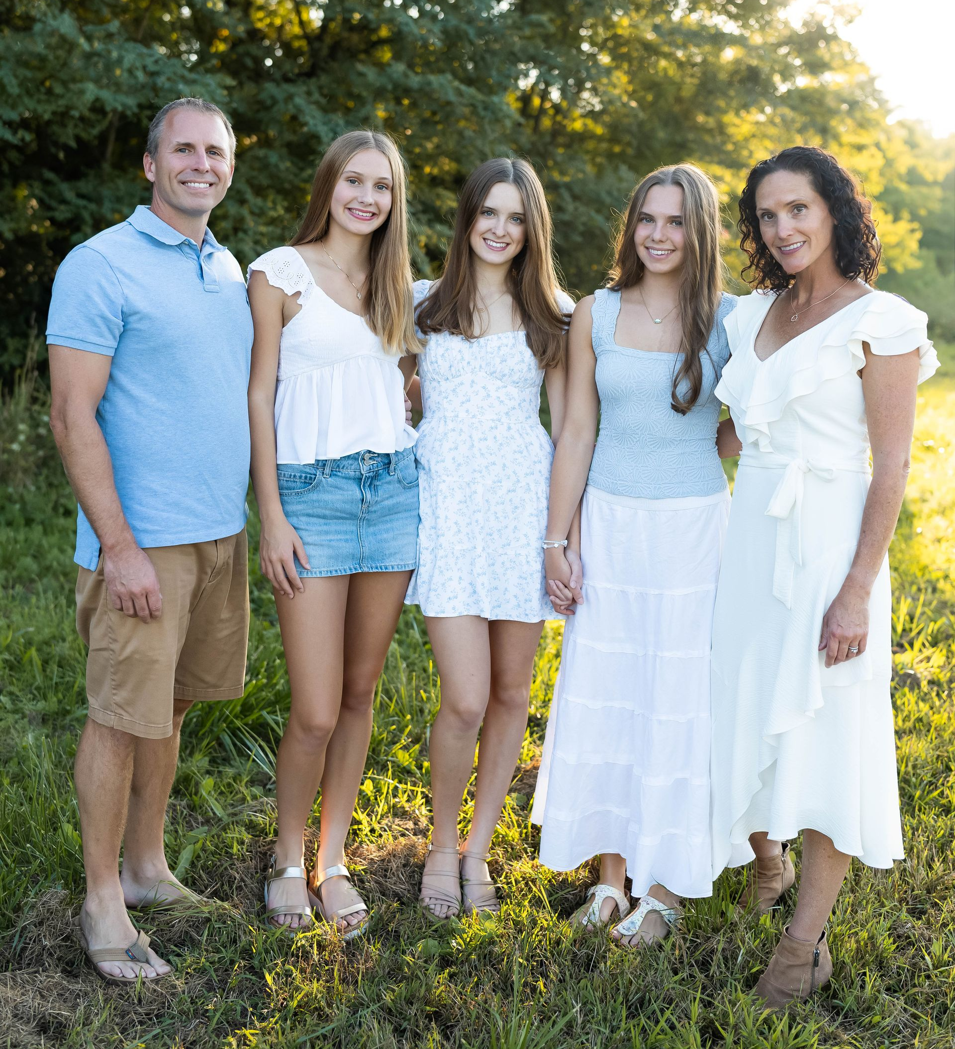 Family of five in nature; smiling, posing. Woman in white dress, man in blue shirt and shorts.