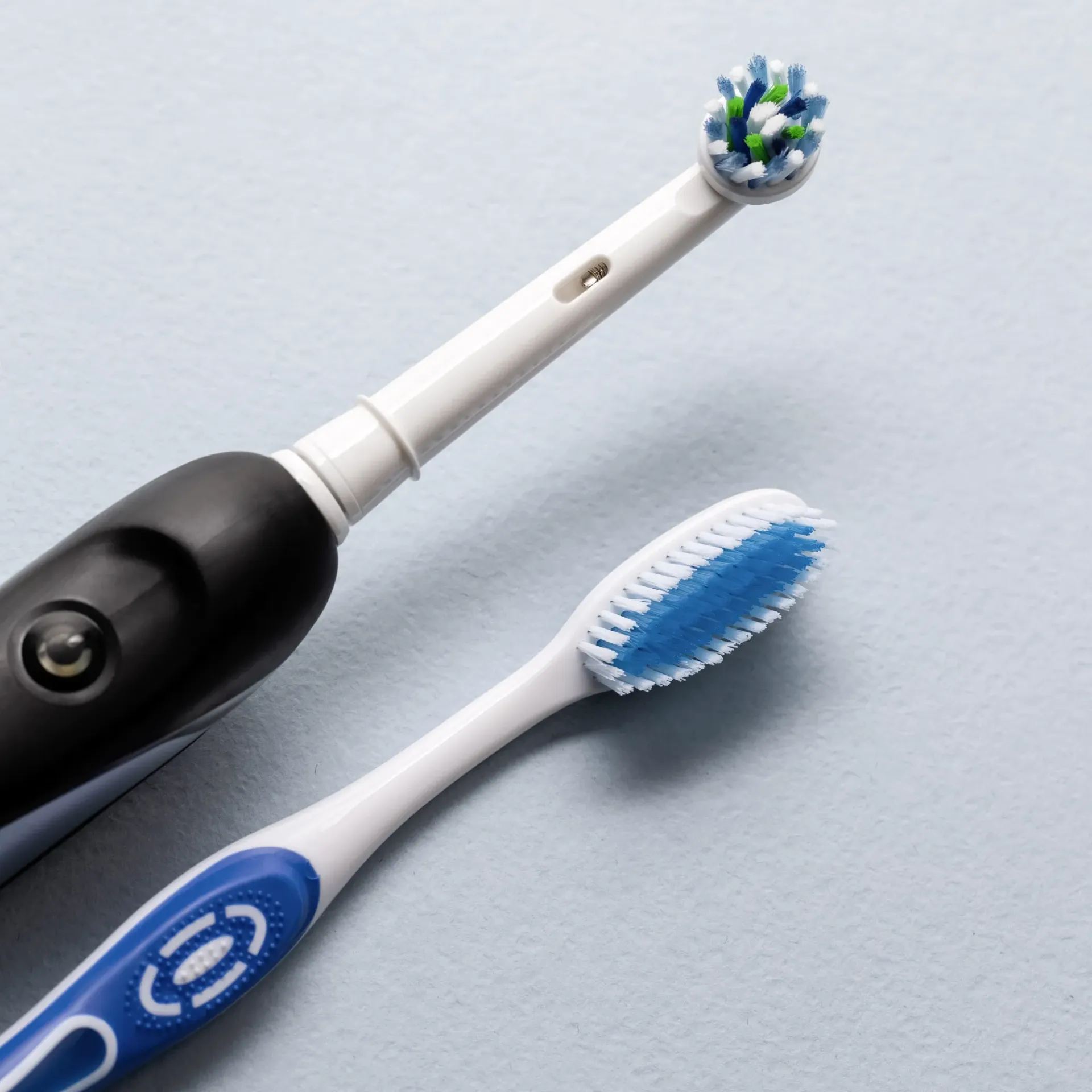 An electric toothbrush and a regular toothbrush are on a table.