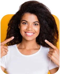 A woman with curly hair is smiling and pointing at her teeth.