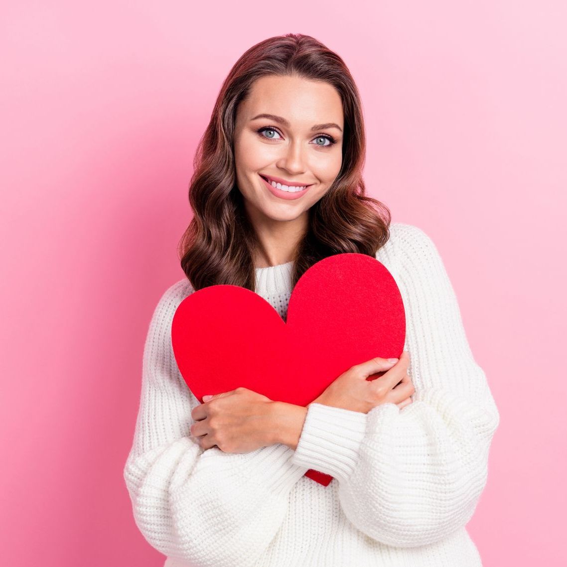 A woman in a white sweater is holding a red heart.