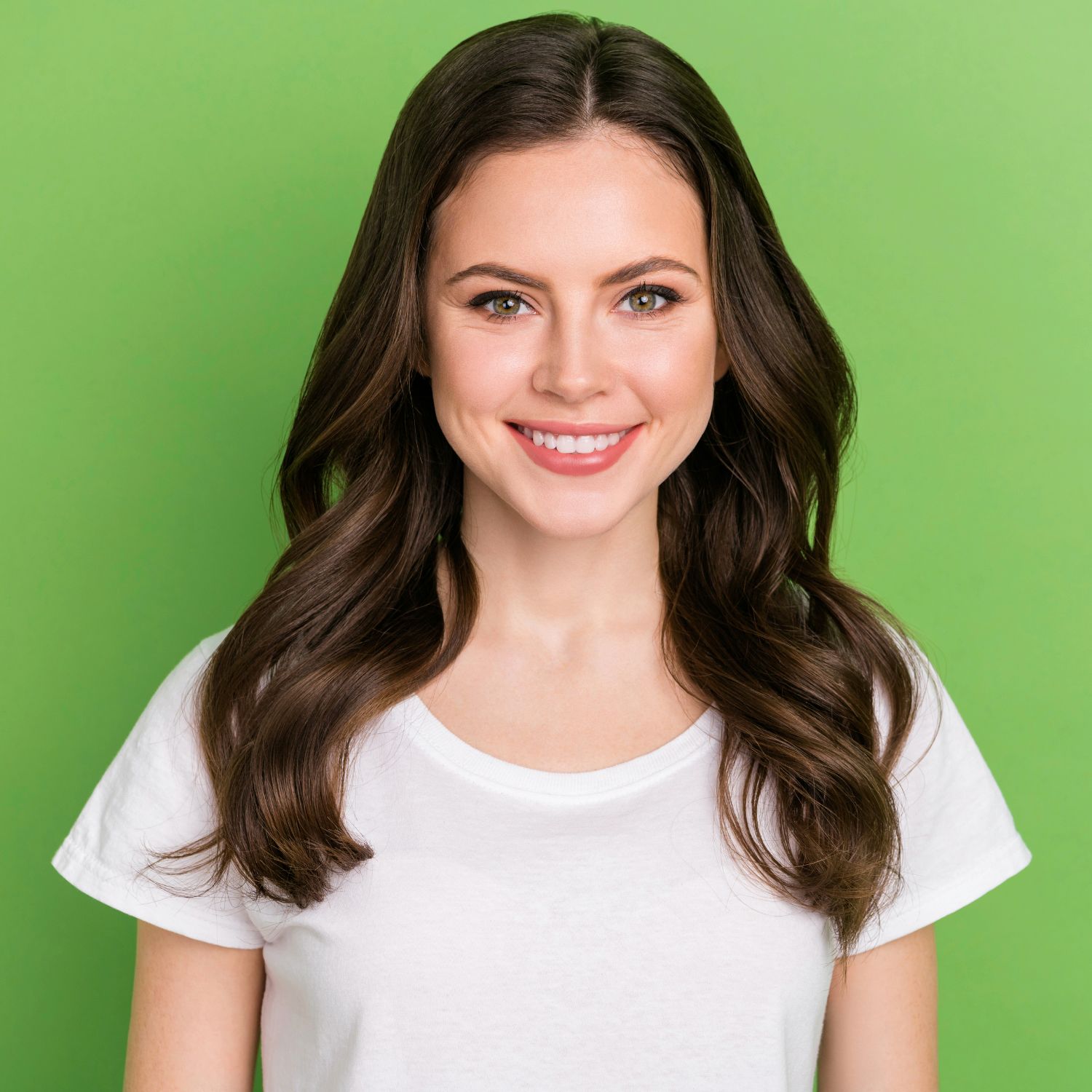 A woman with long brown hair is wearing a white t-shirt and smiling.