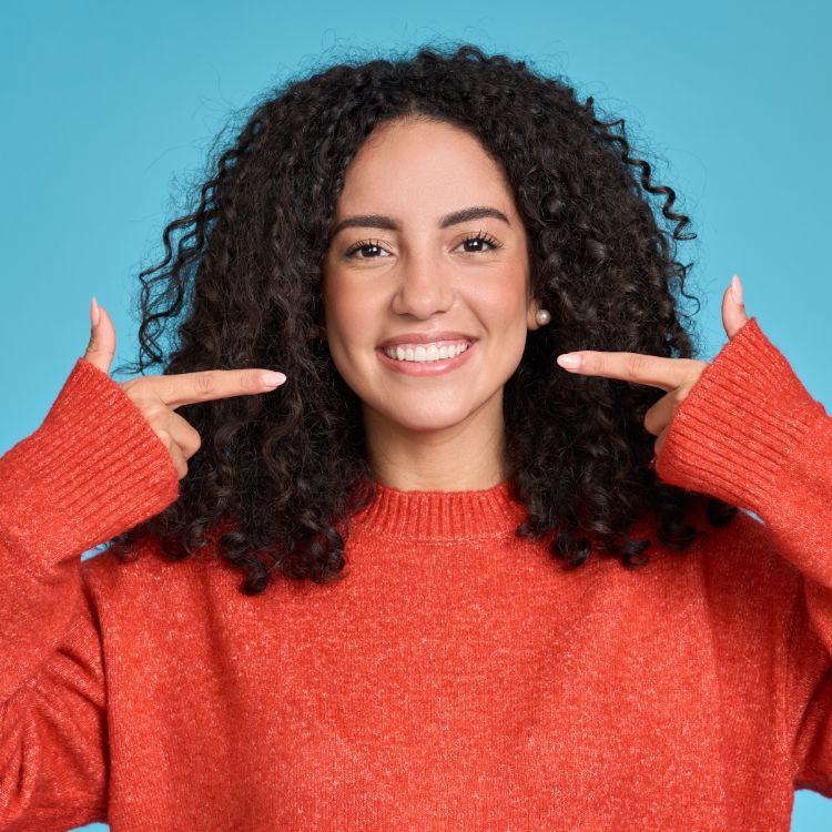 A woman with curly hair is wearing a red sweater and pointing at herself.