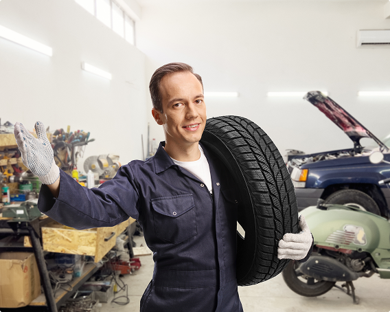 Mechanic holding a tire, smiling, inside a garage with car and scooter. | Morin Brothers Automotive