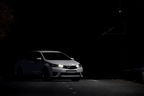 White car with headlights on driving on a dark road at night. | Morin Brothers Automotive