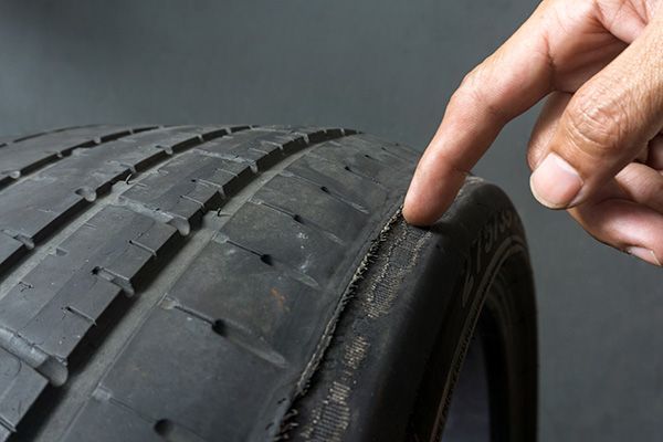 Finger pointing at worn car tire sidewall. | Morin Brothers Automotive