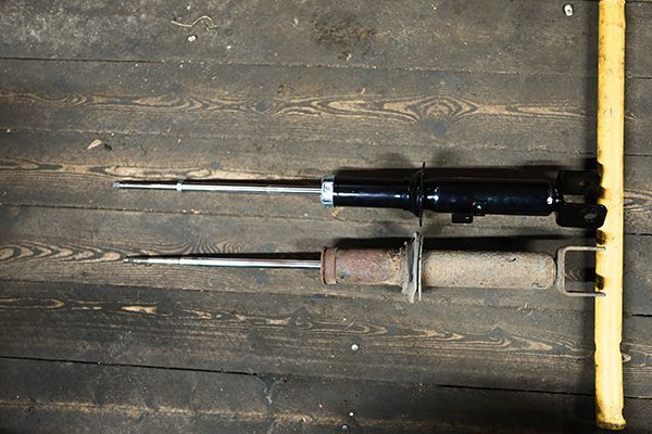Two car shock absorbers, one new and black, the other old and rusted, on a wooden surface. | Morin Brothers Automotive