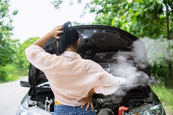 Woman with car hood open, steam rising. Roadside, outdoors, appears distressed. | Morin Brothers Automotive