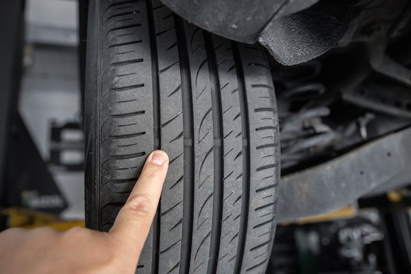 Person's finger pointing at a car tire's tread, in a garage setting. | Morin Brothers Automotive