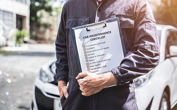 Mechanic holding a clipboard with a car maintenance checklist next to a white car. | Morin Brothers Automotive