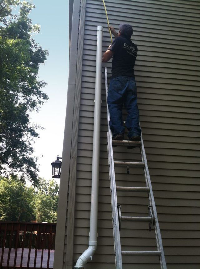 A Man on a Ladder Measuring a Pipe - Youngstown, OH - Radon Raiders
