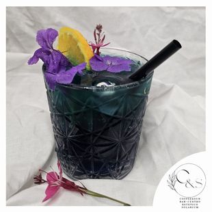 Un bicchiere di liquido blu con fiori viola e una cannuccia