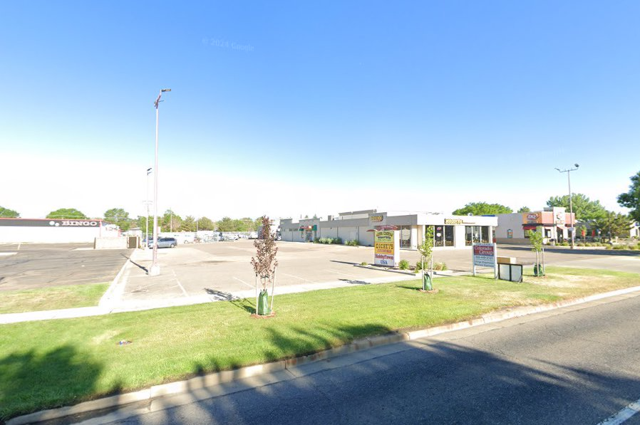 A parking lot next to a road with a building in the background.