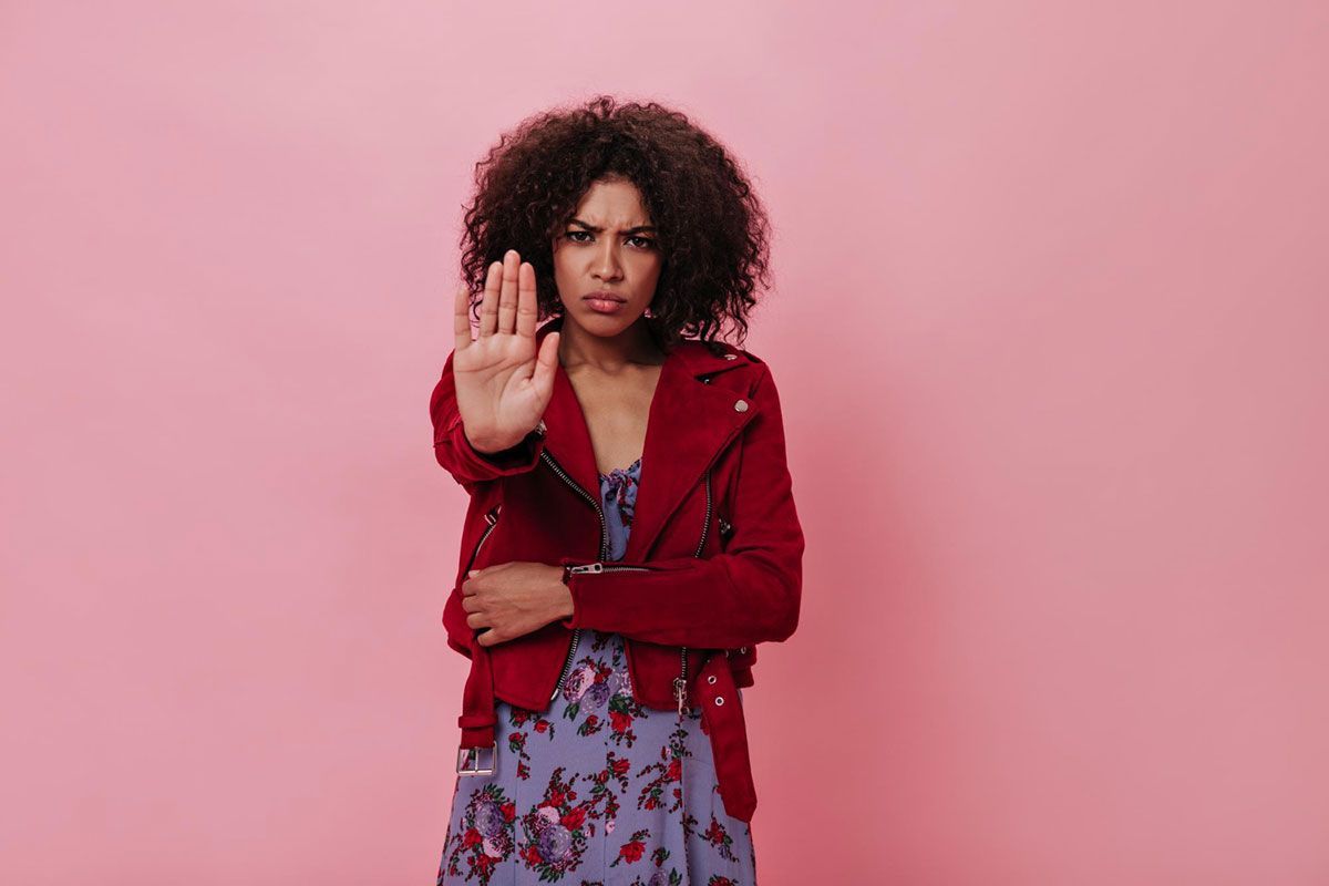 A woman in a red jacket is making a stop sign with her hand.
