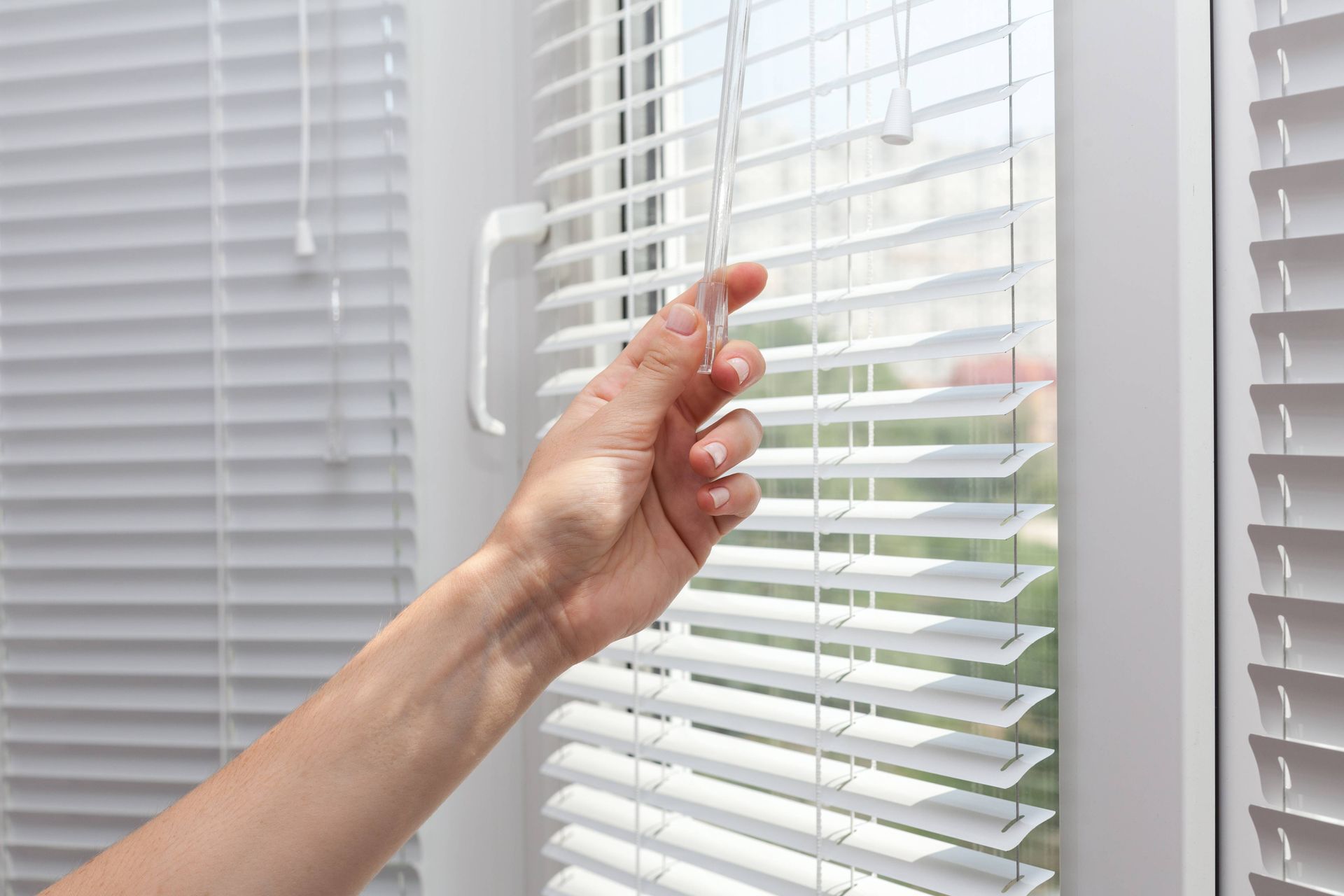 A person's hand twisting open a set of white window blinds at NH Blinds near Manchester, NH