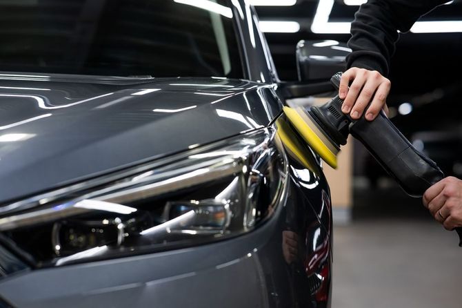 A man is polishing a car with a polisher in a garage.