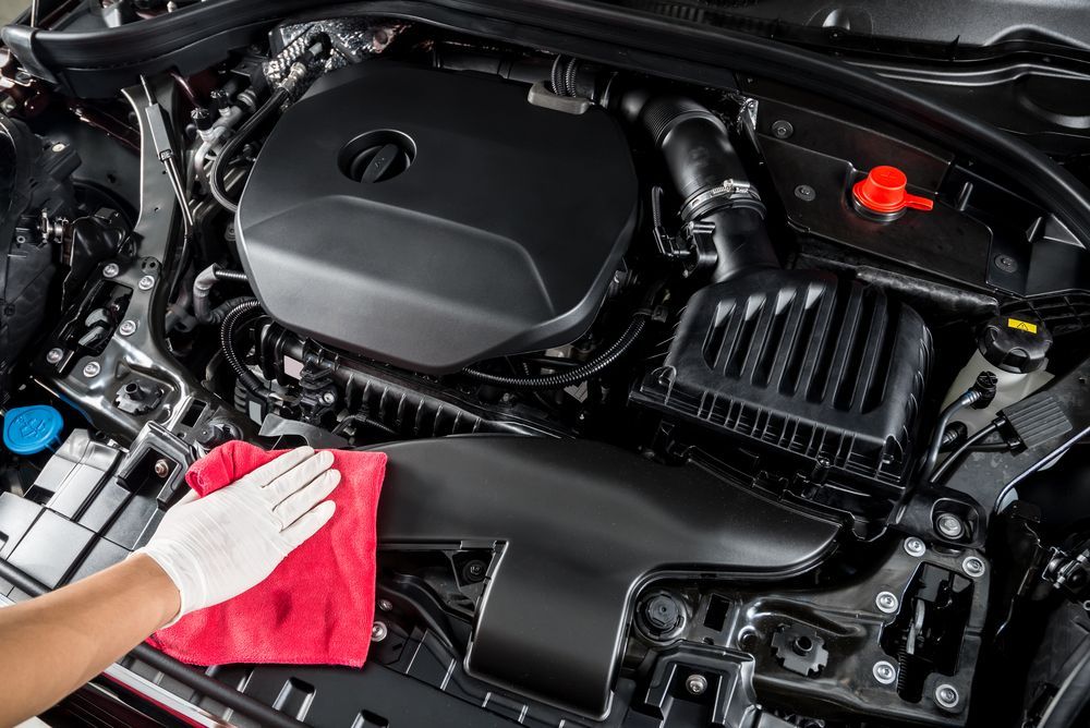 A person is cleaning the engine of a car with a towel.