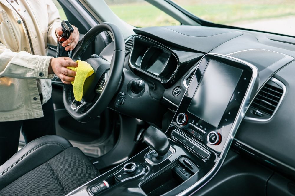 A woman is cleaning the interior of a car with a cloth.
