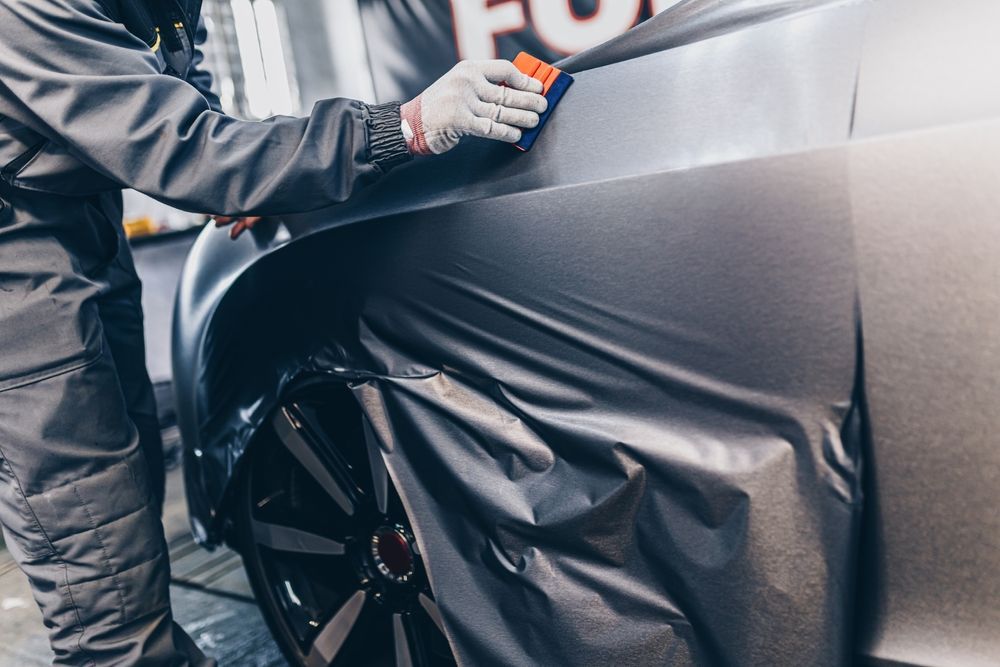 A man is wrapping a car in black vinyl wrap.